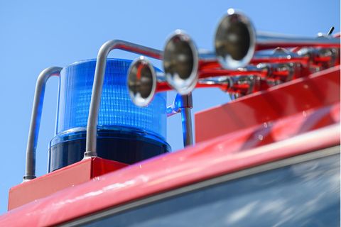 Vor blauem Himmel ist ein Blaulicht auf einem roten Feuerwehrfahrzeug zu sehen. Daneben drei chromglänzende Signalhörner