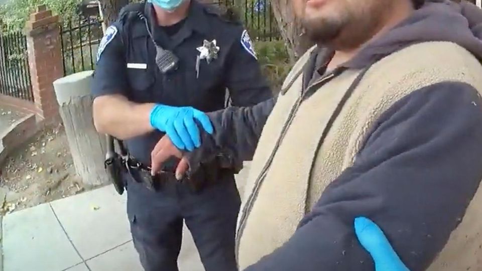 Zwei weiße US-Polizisten halten einen übergewichtigen Latino an beiden Armen. Die Cops tragen blaue OP-Masken und Handschuhe