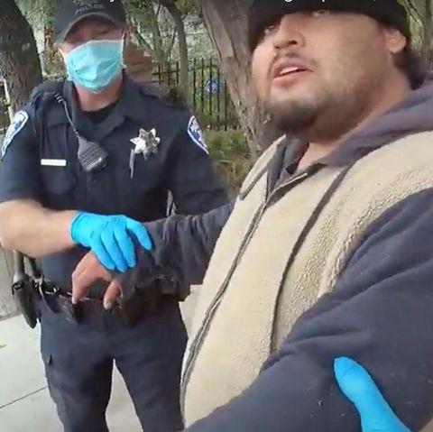 Zwei weiße US-Polizisten halten einen übergewichtigen Latino an beiden Armen. Die Cops tragen blaue OP-Masken und Handschuhe