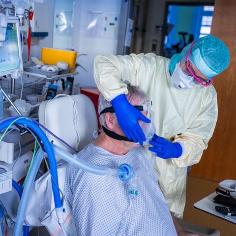 Eine Krankenpflegerin setzt einem Patienten eine Beatmungsmaske auf.