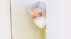 Eine Pflegerin mit Maske und Schutzbrille schaut aus einem Krankenzimmer heraus