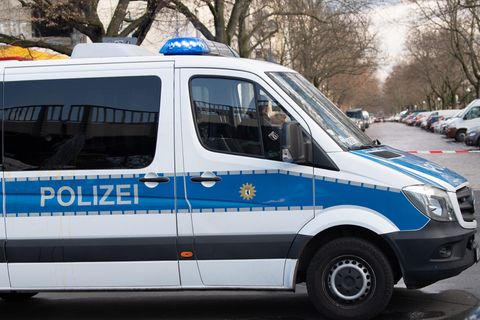 Ein weißer Transporter mit blauem Streifen und "Polizei"-Schriftzug steht quer über die Fahrbahn einer vollgeparkten Straße