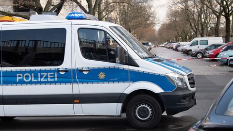 Ein weißer Transporter mit blauem Streifen und "Polizei"-Schriftzug steht quer über die Fahrbahn einer vollgeparkten Straße