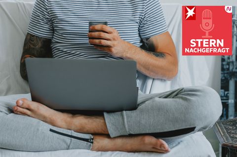 Mann sitzt in Jogginghose und mit Laptop im Bett
