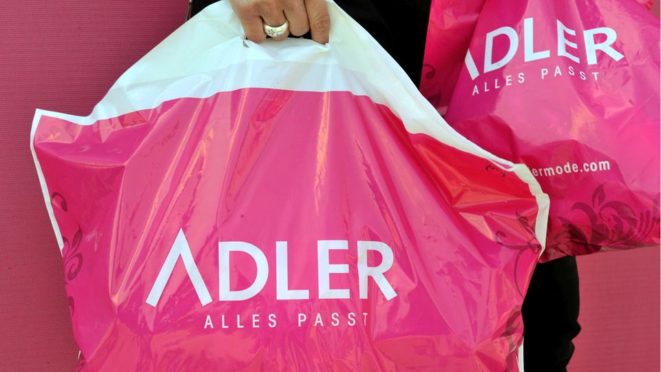 Eine Hand trägt eine Plastiktüte der Textil-Einzelhandelskette Adler Modemärkte