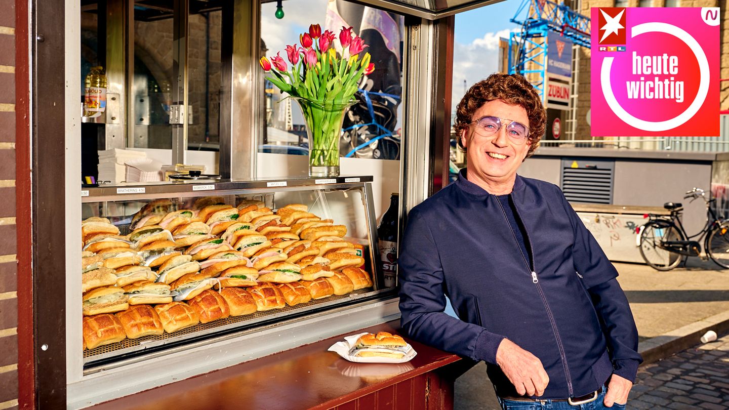 Ein Mann mit braunen Locken und blau getönter Brille lehnt locker am Tresen einer Fischbrötchen-Bude