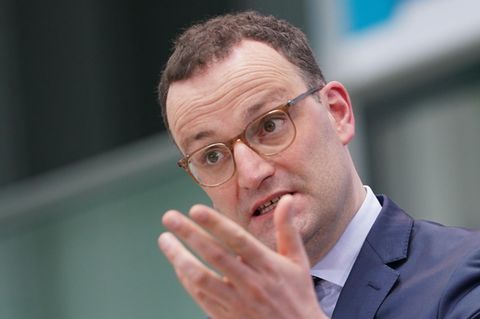 Ein weißer Mann mit kurzen braunen Locken steht in blauem Anzug an einem Rednerpult und gestikuliert mit der linken Hand