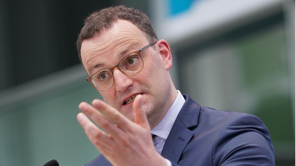 Ein weißer Mann mit kurzen braunen Locken steht in blauem Anzug an einem Rednerpult und gestikuliert mit der linken Hand
