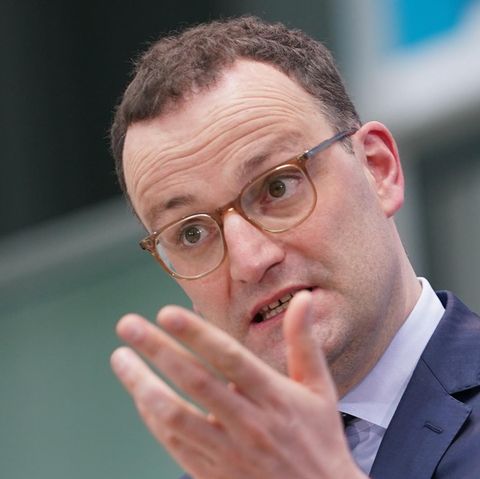 Ein weißer Mann mit kurzen braunen Locken steht in blauem Anzug an einem Rednerpult und gestikuliert mit der linken Hand