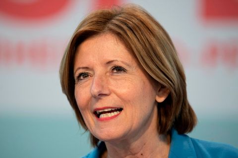 Eine weiße Frau mit schulterlangen, hellbraunen Haaren spricht und lächelt dabei. Sie trägt ein hellblauen Blazer