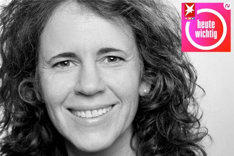 Eine weiße Frau mit langem, gewelltem Haar lächelt auf einem Schwarz-Weiß-Foto