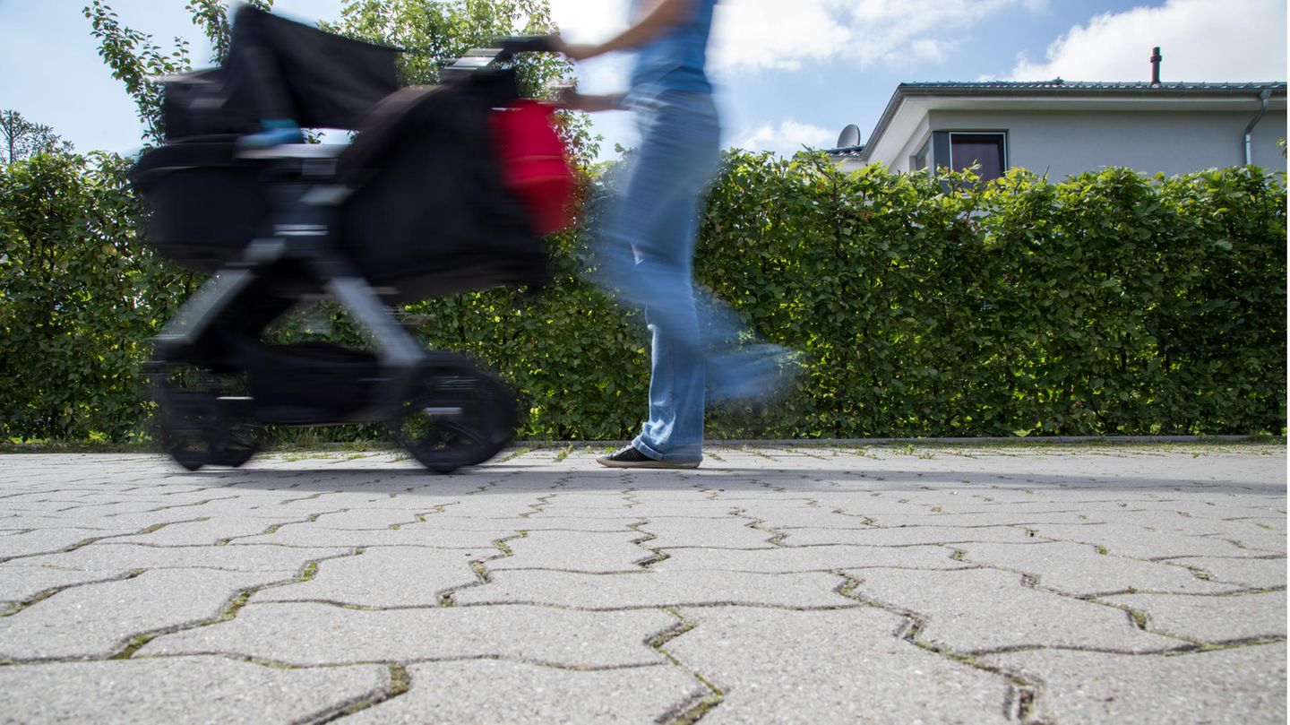 Eine Frau läuft mit Kinderwagen über den Asphalt
