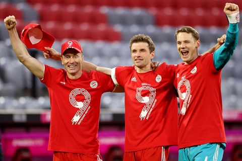 In roten T-Shirts mit einer weißen 9 und dem Wappen des FC Bayern München stehen drei Fußballer Arm in Arm jubelnd im Stadion
