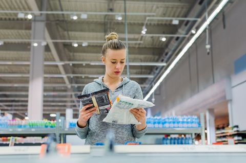 Eine Frau liest im Supermarkt die Zutatenlisten von Tiefkühlprodukten.