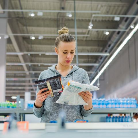 Eine Frau liest im Supermarkt die Zutatenlisten von Tiefkühlprodukten.