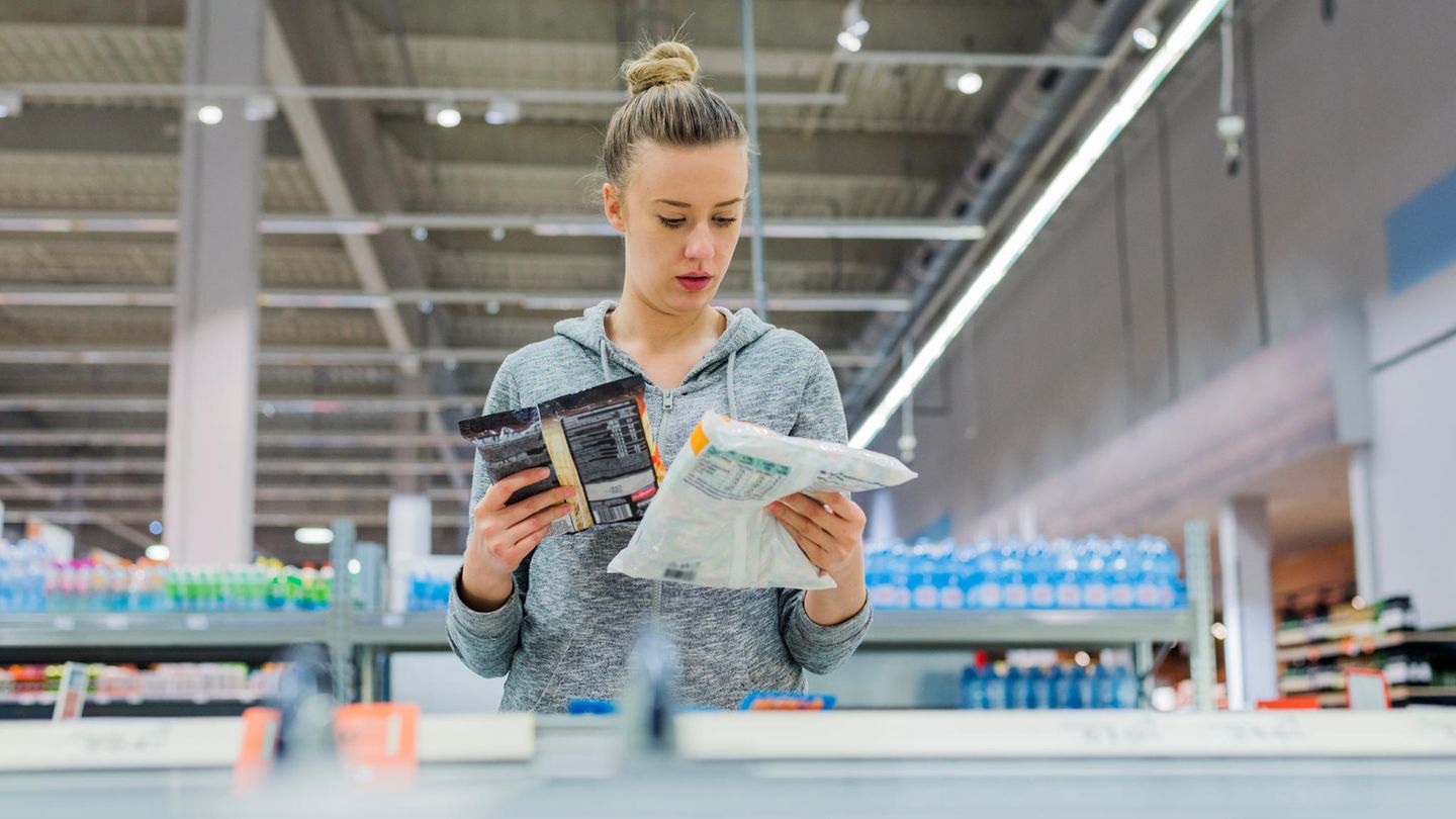 Eine Frau liest im Supermarkt die Zutatenlisten von Tiefkühlprodukten.
