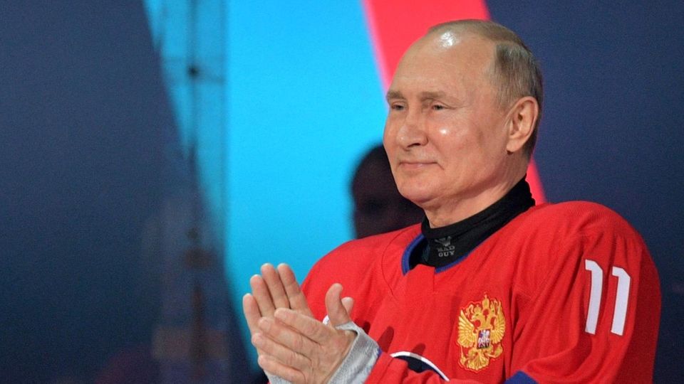 Wladimir Putin steht im Eishockey-Trikot in den russischen Farben auf dem Eis und applaudiert