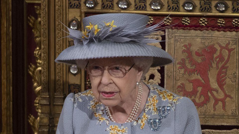 In hellblauem Kostüm mit passendem Hut sitzt Queen Elizabeth II auf einem reich verzierten Holzstuhl im britischen Parlament
