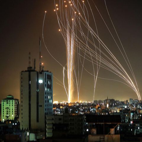 Durch den Nachthimmel über einer Stadt ziehen sich Lichtspuren von Raketen, die von zwei Orten am Horizont starten