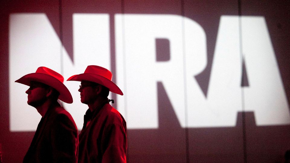 Two people walk past a lettering of the NRA