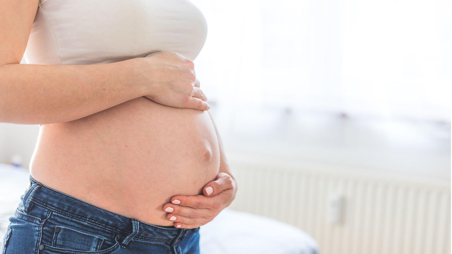 Eine schwangere Frau umfasst ihren Bauch