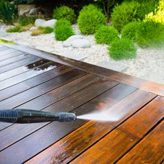 Terrasse reinigen: Wasserstrahl aus einem Hochdruckreiniger trifft auf Holzbohlen einer Terrasse