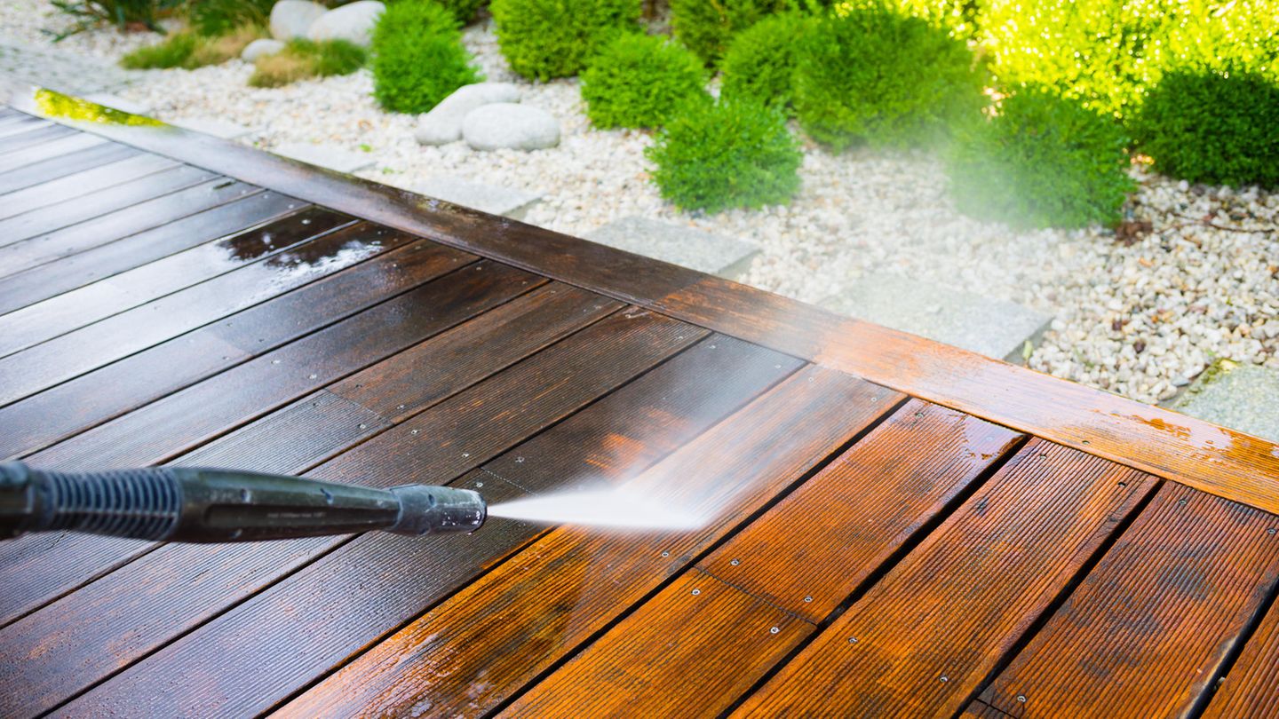 Terrasse reinigen: Wasserstrahl aus einem Hochdruckreiniger trifft auf Holzbohlen einer Terrasse