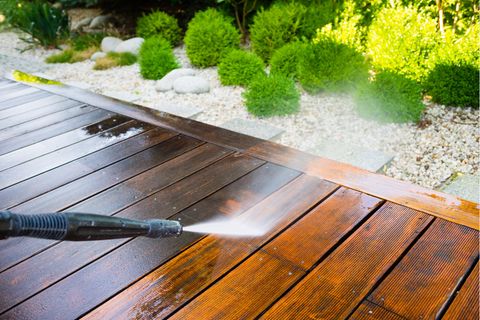 Terrasse reinigen: Wasserstrahl aus einem Hochdruckreiniger trifft auf Holzbohlen einer Terrasse