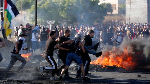 Männer tragen inmitten von Krawallen einen Mann, im Hintergrund ist ein Feuer zu sehen