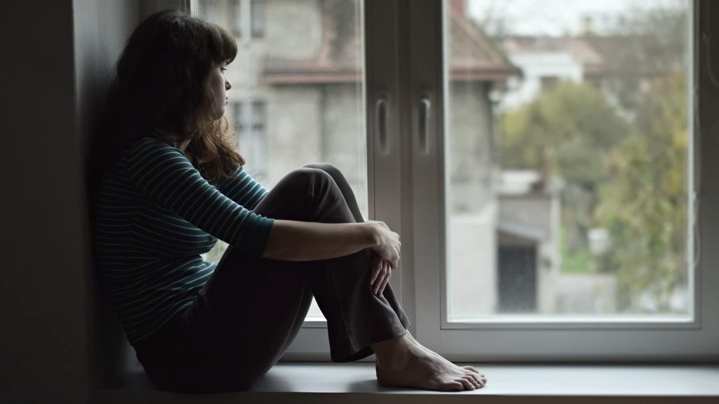 Junge Frau sitzt traurig am Fenster