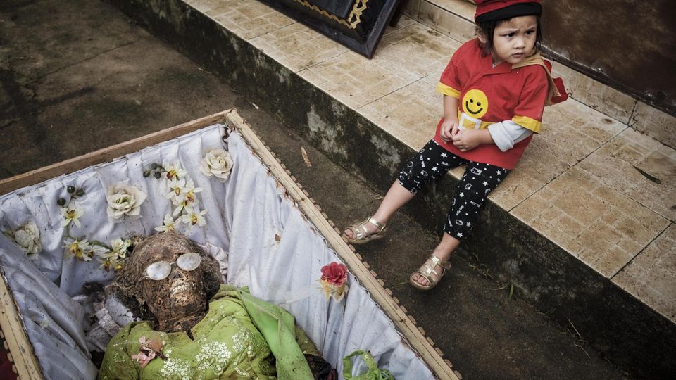 Indonesien  Ist die Reisernte beendet, kommt für einige indonesische Gemeinden der Moment der Ma’nene-Zeremonie. Dann begibt man sich zum Friedhof und hebt die Verstorbenen aus ihren Gräbern. Erst reinigt man die in Formaldehyd konservierten Toten, dann zieht man ihnen ihre besten Kleider an. Nachdem man die Ahnen in der Sonne getrocknet hat, macht man ein Erinnerungsfoto mit ihnen.