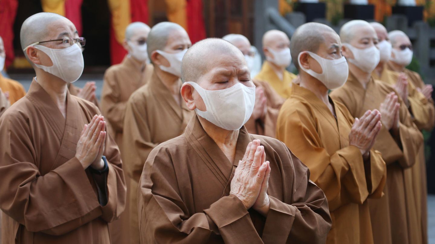 Buddhistische Mönche und Nonnen, die wegen der Corona-Krise einen Mund-Nasen-Schutz tragen, beten gemeinsam Buddhistische Mönche und Nonnen, die wegen der Corona-Krise einen Mund-Nasen-Schutz tragen, beten gemeinsam