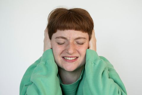 Frau hält sich beide Ohren zu