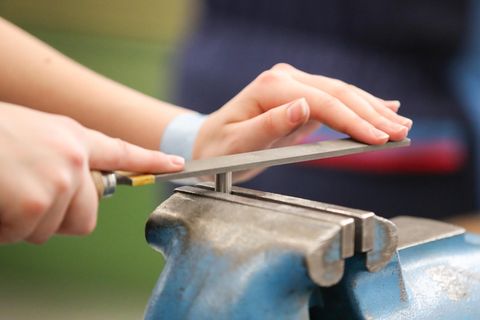 Die Hände einer jungen Frau führen eine Feile über ein in blauem Schraubstock eingespannten Metallstift