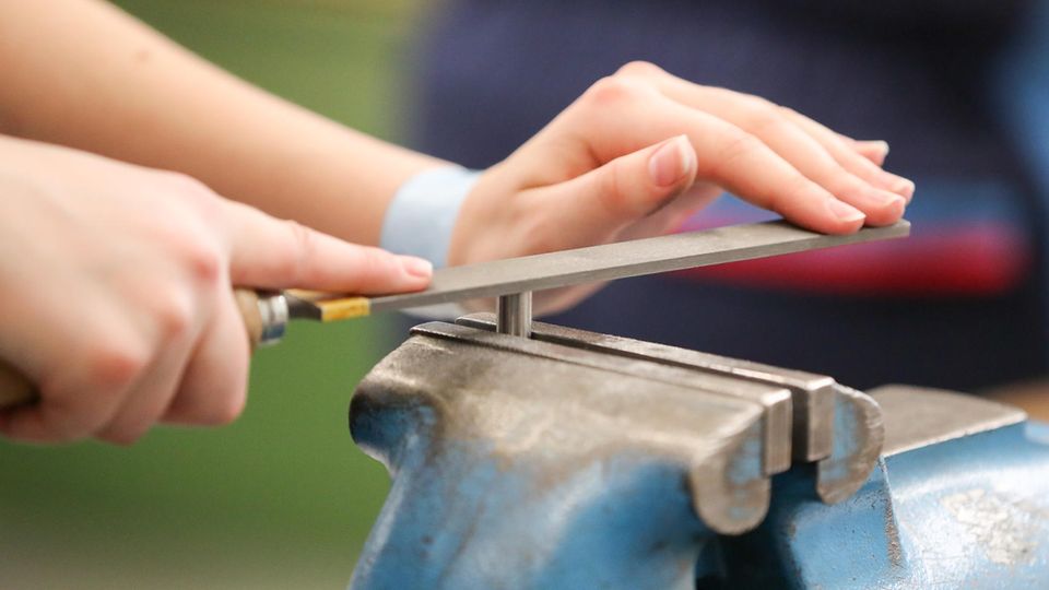 Die Hände einer jungen Frau führen eine Feile über ein in blauem Schraubstock eingespannten Metallstift