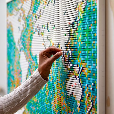 Lego World Map: Frauenhand steckt einen Pin auf die Lego Weltkarte