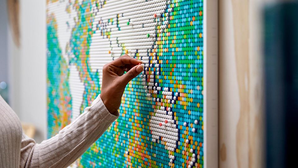 Lego World Map: Frauenhand steckt einen Pin auf die Lego Weltkarte