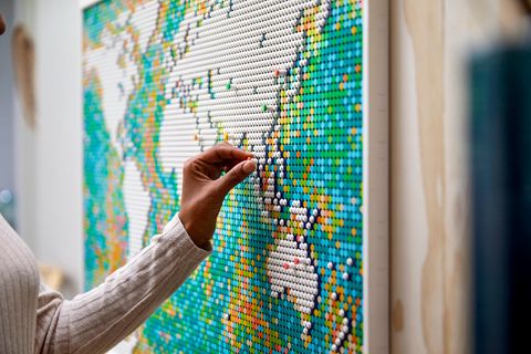 Lego World Map: Frauenhand steckt einen Pin auf die Lego Weltkarte