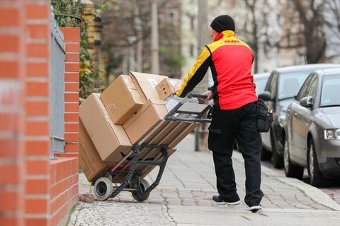 DHL-Zusteller mit einer Sackkarre voller Pakete.