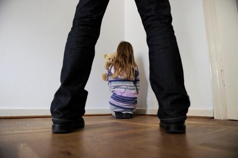 Ein Mann steht hinter einem Kind, das sich in einer Ecke verkrochen hat (Symbolbild)
