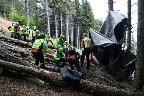 Am Rande einer Lichtung in einem Bergwald stehen Rettungskräfte in neongrünen Helmen und Jacken vor den Trümmern einer Gondel