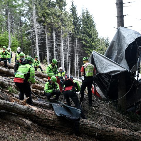 Am Rande einer Lichtung in einem Bergwald stehen Rettungskräfte in neongrünen Helmen und Jacken vor den Trümmern einer Gondel