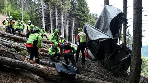 Am Rande einer Lichtung in einem Bergwald stehen Rettungskräfte in neongrünen Helmen und Jacken vor den Trümmern einer Gondel