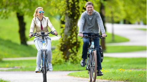 Ein Paar fährt auf E-Bikes durch einen Park