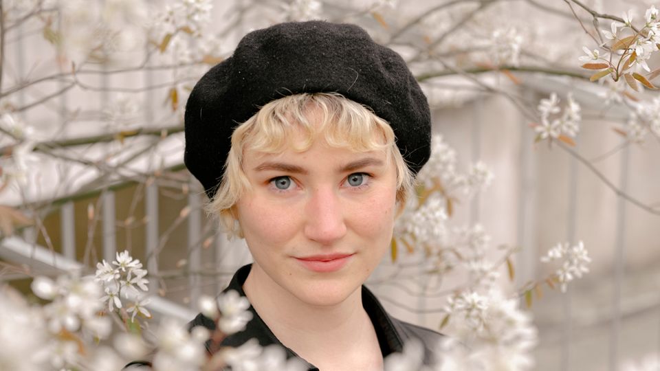 Sophia Sailer Sophia Sailer hat kurze blonde Haare und posiert hinter Blumen