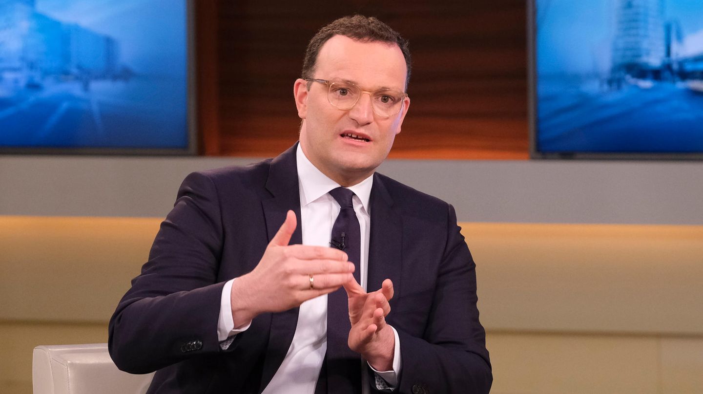 Ein Mann mit Brille und braunen Locken sitzt im Anzug in einem TV-Studio und gestikuliert mit beiden Händen vor der Brust