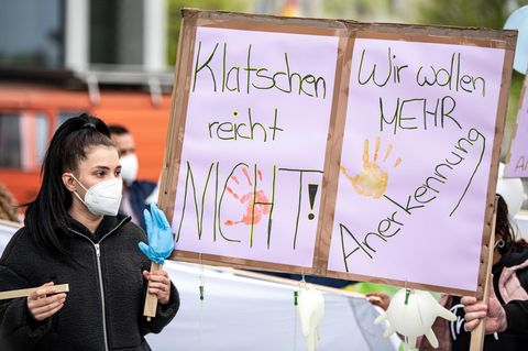 Eine Pflegekraft hält ein Protestschild in die Höhe