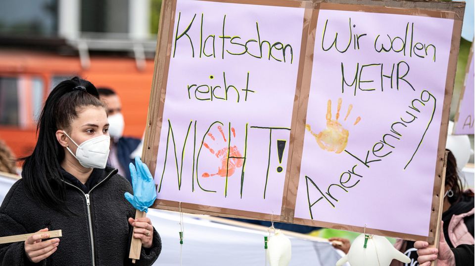 Eine Pflegekraft hält ein Protestschild in die Höhe