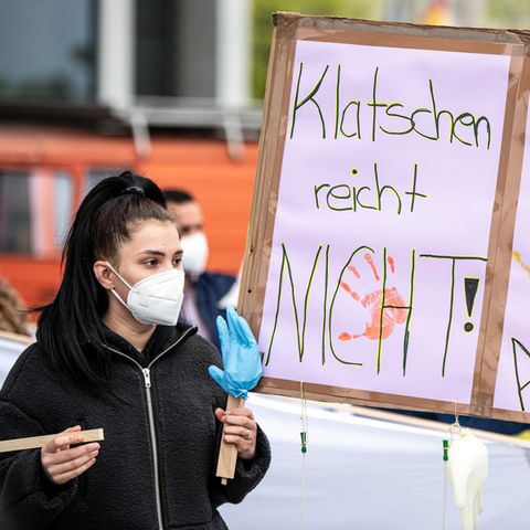 Eine Pflegekraft hält ein Protestschild in die Höhe