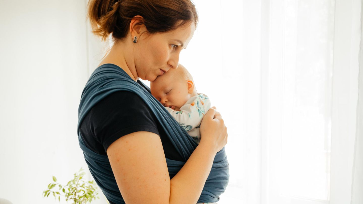 Eine junge Mutter trägt ihr Baby in einem Tragetuch vor der Brust